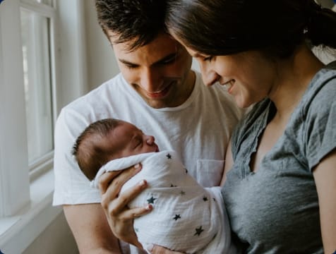 A smiling couple holds an infant wrapped in a blanket