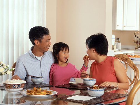 A family of three seated at their dining room table eating a meal and smiling